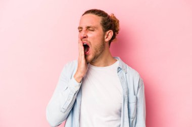 Pembe arka planda izole edilmiş genç beyaz adam esniyor. Ağzı eliyle kapatan yorgun bir hareket sergiliyor..