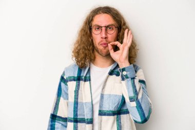 Beyaz arka planda izole edilmiş beyaz tenli genç bir adam parmakları dudaklarında bir sır saklıyor..