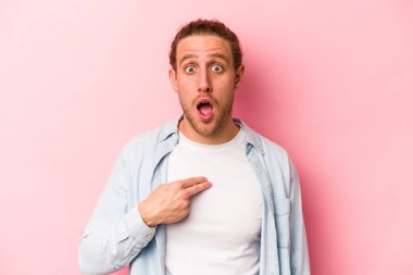Pembe arka planda izole edilmiş genç beyaz adam parmağını göstererek şaşırdı, geniş bir gülümsemeyle..