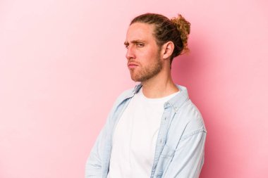 Pembe arka planda izole edilmiş genç beyaz adam şüpheli, belirsiz, seni muayene ediyor..
