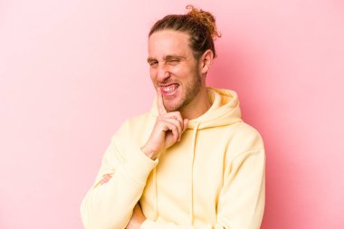 Pembe arka planda izole edilmiş genç beyaz adam gülümsüyor ve kendinden emin, elleriyle çenesine dokunuyor..