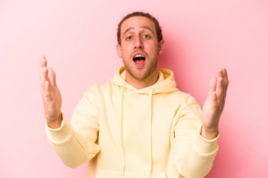 Pembe arka planda izole edilmiş genç beyaz bir adam zaferi ya da başarıyı kutluyor, şaşırıyor ve şok oluyor..