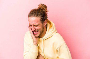 Pembe arka planda izole edilmiş genç beyaz adam mutlu bir şekilde gülüyor ve ellerini karnının üstünde tutarak eğleniyor..