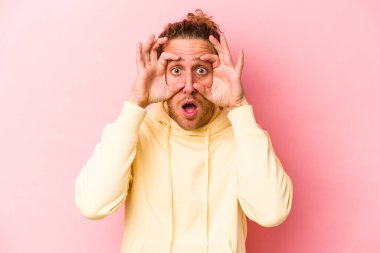 Pembe arka planda izole edilmiş genç beyaz adam bir başarı fırsatı bulmak için gözlerini açık tutuyor..