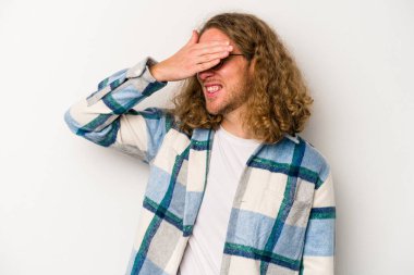 Beyaz arka planda soyutlanmış beyaz tenli genç bir adam elleriyle gözlerini kapatıyor, geniş bir gülümsemeyle bir sürpriz bekliyor..