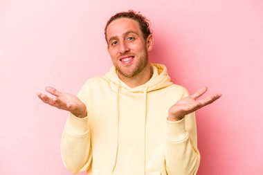 Pembe arka planda izole edilmiş genç beyaz adam kollarıyla ölçek oluşturuyor, mutlu ve kendinden emin hissediyor..