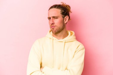 Pembe arka planda izole edilmiş genç beyaz adam alaycı bir ifadeyle kameraya bakıyor..
