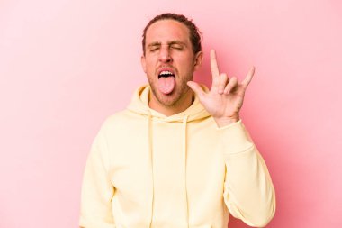 Pembe arka planda izole edilmiş genç beyaz adam parmaklarıyla taş hareketi gösteriyor.