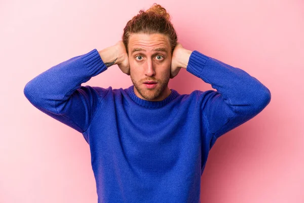 Kafkasyalı genç adam pembe arka planda izole edilmiş kulakları kulaklarıyla kapatıyor çok fazla ses duymamaya çalışıyor..