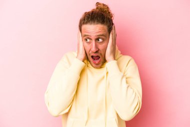 Kafkasyalı genç adam pembe arka planda izole edilmiş kulakları kulaklarıyla kapatıyor çok fazla ses duymamaya çalışıyor..