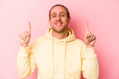 Pembe arka planda izole edilmiş genç beyaz adam iki parmağı da boş bir alan gösteriyor..
