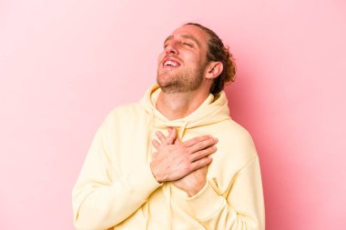 Pembe arka planda izole olmuş genç beyaz adam gülüyor, elini yüreğine koyuyor, mutluluk kavramını koruyor..