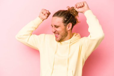 Pembe arka planda soyutlanmış genç beyaz adam özel bir günü kutluyor, atlıyor ve enerjiyle kollarını kaldırıyor..