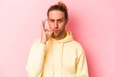 Pembe arka planda izole edilmiş genç beyaz bir adam parmakları dudaklarında bir sır saklıyor..