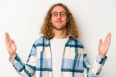 Beyaz arka planda izole edilmiş genç beyaz bir adam işaret parmaklarıyla küçük bir şey tutuyor, gülümsüyor ve kendinden emin..