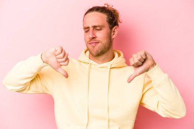 Pembe arka planda izole edilmiş genç beyaz adam baş parmağını aşağı gösteriyor, hayal kırıklığı konsepti..