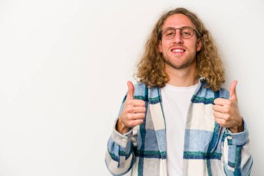 Beyaz arka planda izole edilmiş genç beyaz adam gülümsüyor ve başparmağını kaldırıyor.