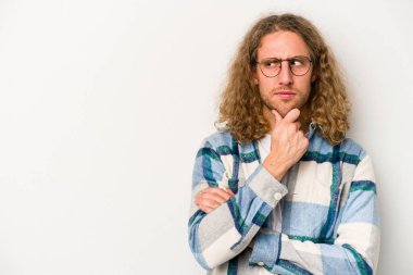 Beyaz arka planda izole edilmiş genç beyaz bir adam şüpheli ve şüpheci bir ifadeyle yana bakıyor..