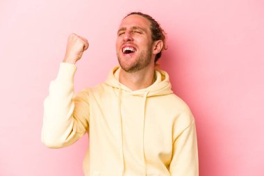 Pembe arka planda izole edilmiş genç beyaz bir adam zaferi, tutkuyu ve coşkuyu kutluyor, mutlu bir ifade..