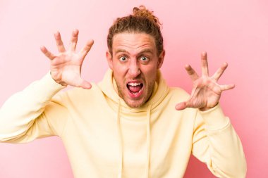 Pembe arka planda izole edilmiş genç beyaz adam pençelerini kedi taklidi yaparken gösteriyor, agresif bir hareket..