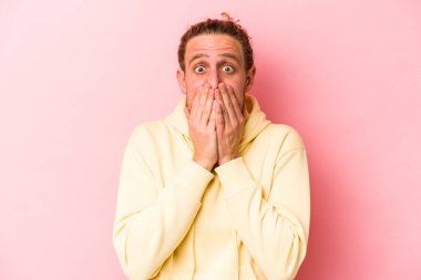 Pembe arka planda izole edilmiş genç beyaz adam şok olmuş, ağzı ellerle kaplanmış, yeni bir şey keşfetmeye hevesli..