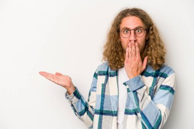 Beyaz arka planda izole edilmiş genç beyaz adam, avuç içi fotokopi alanını elinde tutmaktan etkilenmiş..