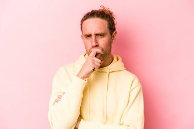 Kafkasyalı genç adam pembe arka planda izole edilmiş düşünüyor ve yukarı bakıyor, yansıtıyor, düşünüyor, bir fantezi kuruyor..