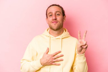 Pembe arka planda izole edilmiş genç beyaz adam yemin ediyor, elini göğsüne koyuyor..