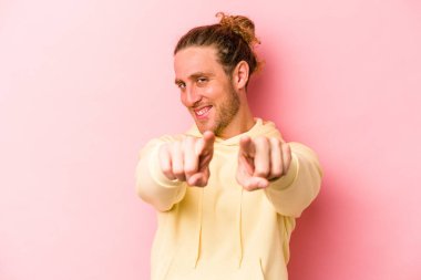 Pembe arka planda izole edilmiş genç beyaz adam parmaklarıyla ön tarafı işaret ediyor..