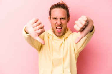 Pembe arka planda izole edilmiş genç beyaz adam baş parmağını aşağı gösteriyor ve hoşlanmadığını ifade ediyor..