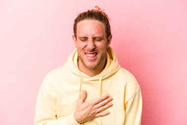 Pembe arka planda izole edilmiş genç beyaz adam yüksek sesle gülüyor elini göğsünde tutuyor..