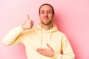 Pembe arka planda izole edilmiş genç beyaz adam karnına dokunuyor, nazikçe gülümsüyor, yemek yiyor ve tatmin oluyor..