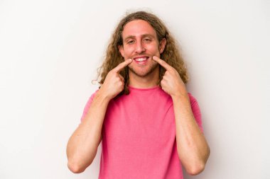 Beyaz arka planda izole edilmiş genç beyaz adam gülümsüyor, parmaklarını ağıza doğrultuyor..