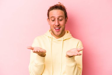 Pembe arka planda izole edilmiş genç beyaz bir adam elinde avuç içi bir şeyle kameraya sunuyor..