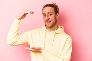 Pembe arka planda izole edilmiş genç beyaz adam işaret parmaklarıyla küçük bir şey tutuyor, gülümsüyor ve kendinden emin..