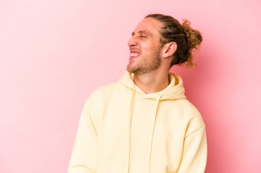 Genç beyaz adam pembe arka planda izole edilmiş rahat ve mutlu bir şekilde gülüyor, boynunda dişlerini gösteriyor..