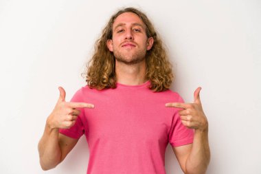 Beyaz arka planda yaşayan beyaz tenli genç bir adam gömlek fotokopi alanını gösteriyor, gururlu ve kendinden emin.