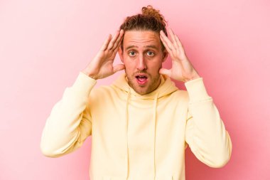 Pembe arka planda izole edilmiş genç beyaz adam hoş bir sürpriz alıyor, heyecanlı ve el kaldırıyor..