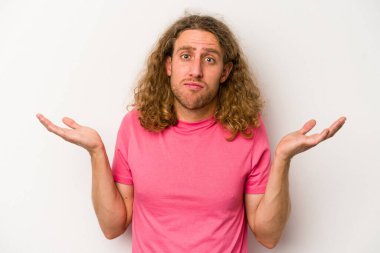 Beyaz arka planda izole edilmiş genç beyaz bir adam sorgulama sırasında omuz silkiyor ve şüphe duyuyor..