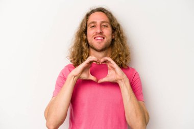 Beyaz arka planda izole edilmiş genç beyaz bir adam gülümsüyor ve elleriyle kalp şekli gösteriyor..