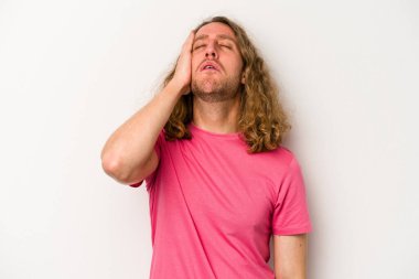 Beyaz arka planda izole edilmiş genç beyaz bir adam yorgun ve uykulu bir şekilde elini başının üstünde tutuyor..