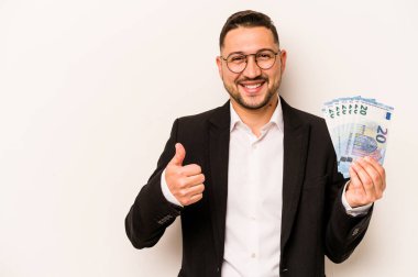 Beyaz arka planda izole edilmiş banknotları tutan İspanyol bir adam gülümsüyor ve başparmağını kaldırıyor.