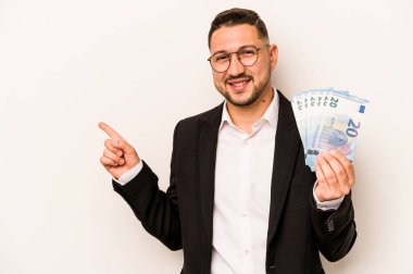 Beyaz arka planda izole edilmiş banknotlar tutan İspanyol bir adam gülümsüyor ve boş alanda bir şeyler gösteriyor..