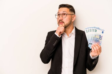 Beyaz arka planda izole edilmiş banknotları tutan İspanyol bir adam şüpheli ve şüpheci bir ifadeyle yana bakıyor..