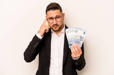 Beyaz arka planda izole edilmiş banknotlar tutan İspanyol bir adam şakağı parmağıyla işaret ediyor, düşünüyor ve bir göreve odaklanıyor..
