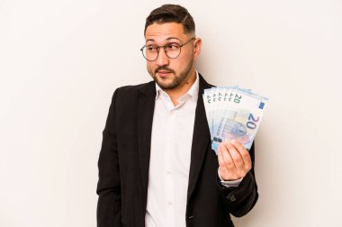 Hispanik adamın elinde banknotlar var. Beyaz arka planda izole edilmiş. Kafası karışık, şüpheci ve kararsız..