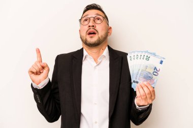 Hispanik adamın elinde banknotlar var. Beyaz arka planda izole edilmiş. Ağzı açık, üst tarafı işaret ediyor..