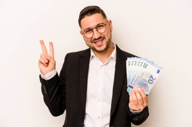 Beyaz arka planda izole edilmiş banknotları tutan İspanyol bir adam neşeli ve kaygısız parmakları olan bir barış sembolü gösteriyor..