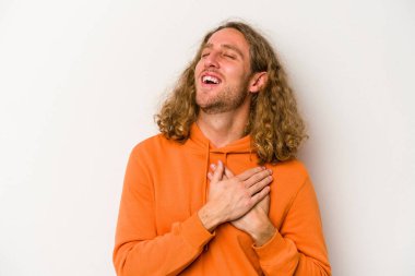 Beyaz arka planda soyutlanmış beyaz tenli genç bir adam gülüyor, elini yüreğine koyuyor, mutluluk kavramını koruyor..