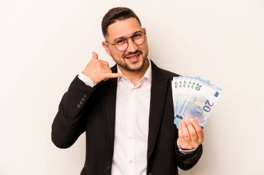 Beyaz arka planda izole edilmiş banknotlar tutan İspanyol bir adam, parmaklarıyla bir cep telefonu görüşmesi jesti gösteriyor..